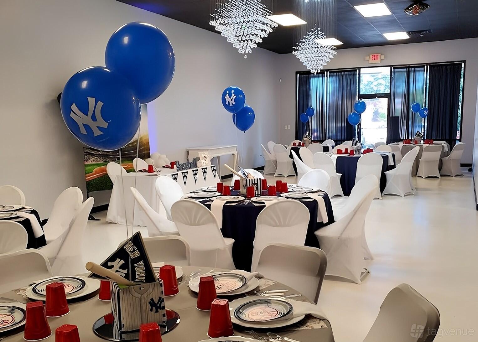 An event venue with white round tables, navy linens, banquet chairs, and blue balloon decorations at Touch of Class Eventz.