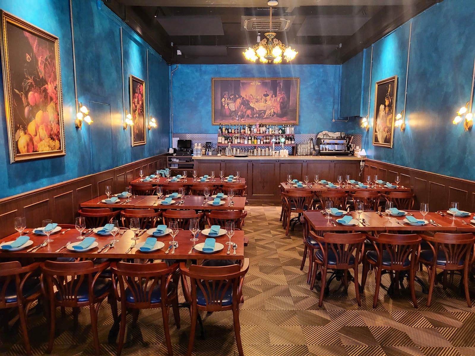 A restaurant with blue walls, wooden tables set with blue napkins, and framed paintings at Quay House.