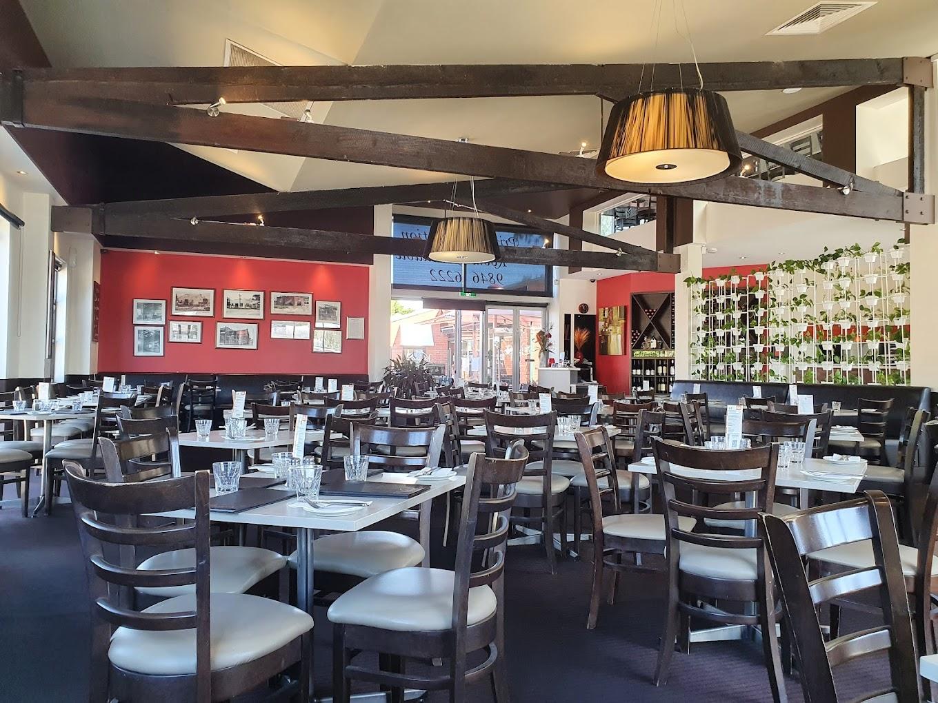 A restaurant with dark wood ceiling beams, framed art on red walls, and set tables with glasses at Vibrante Restaurant.