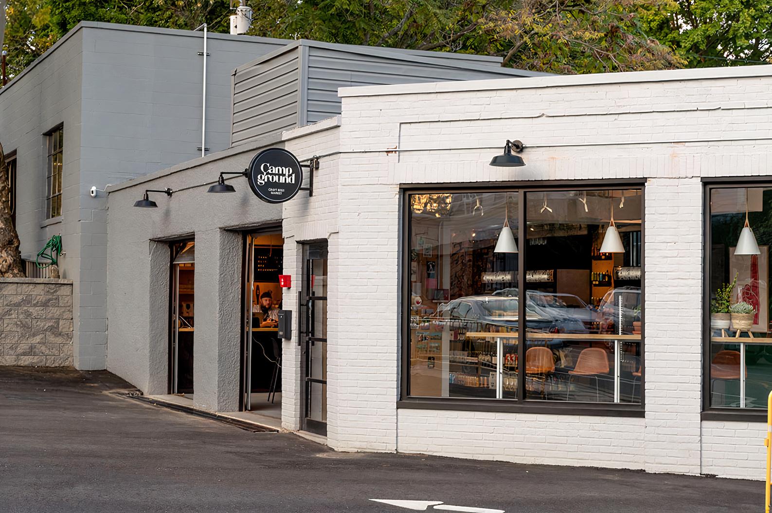 A pub with a white brick exterior, large windows, and outdoor parking at Campground Craft Beer Market.