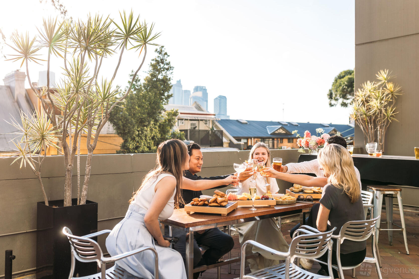 A hotel terrace with potted palms, city views, and guests dining at wooden tables at Holiday Inn Sydney Potts Point.
