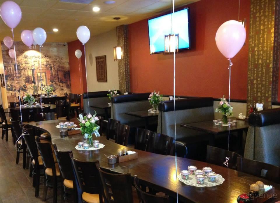 An event space in a restaurant with long wooden tables, booth seating, pink balloons, and floral centerpieces at Crouching Tiger Restaurant & Bar.
