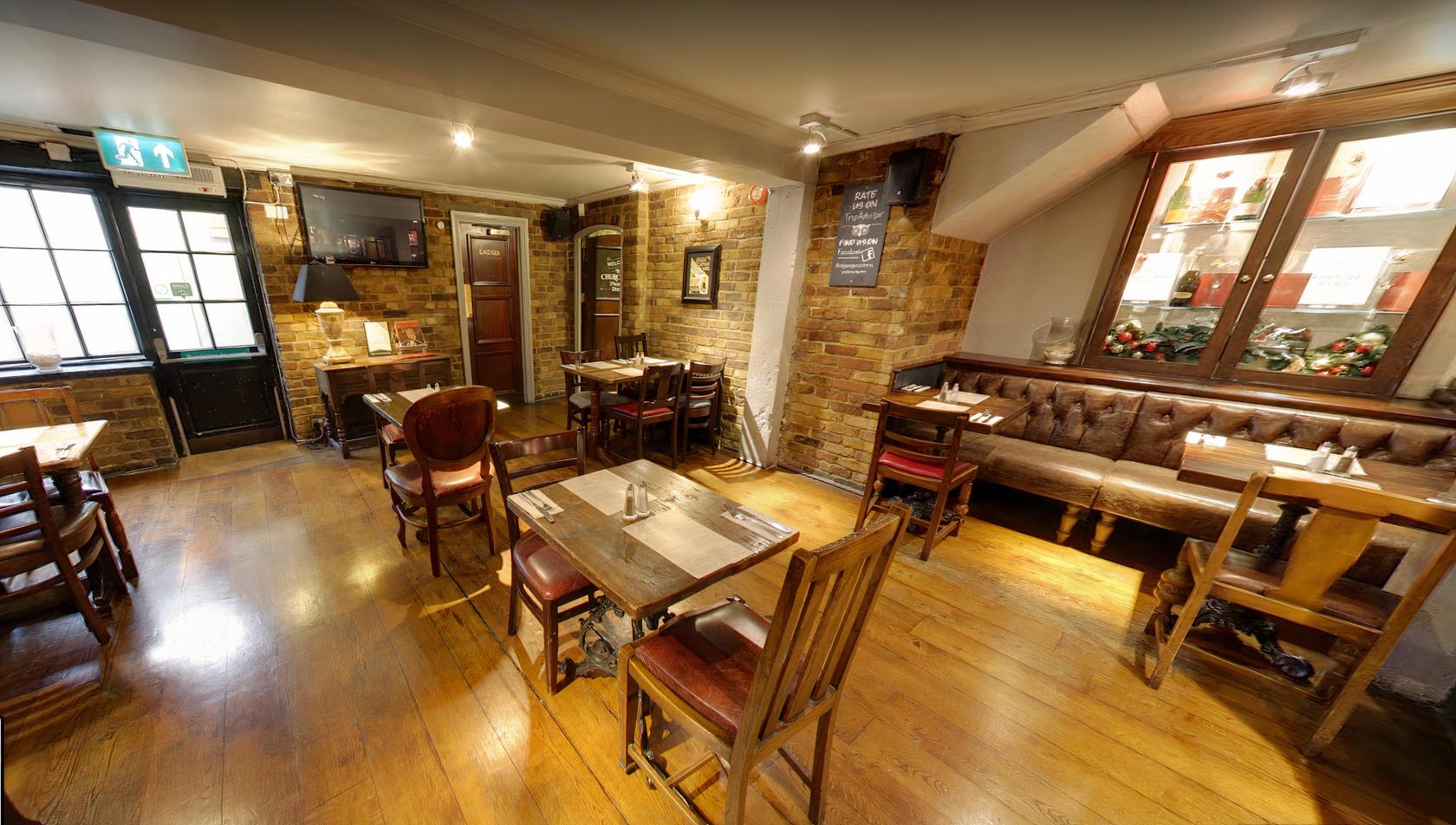A dining room with exposed brick walls, wooden floors, and a mix of wooden tables and leather banquette seating at St Georges Tavern.