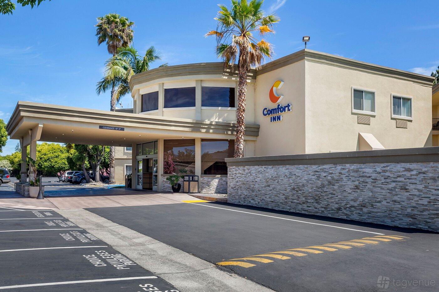 A hotel entrance with covered driveway, palm trees, and stone accent walls at Comfort Inn Sunnyvale - Silicon Valley.