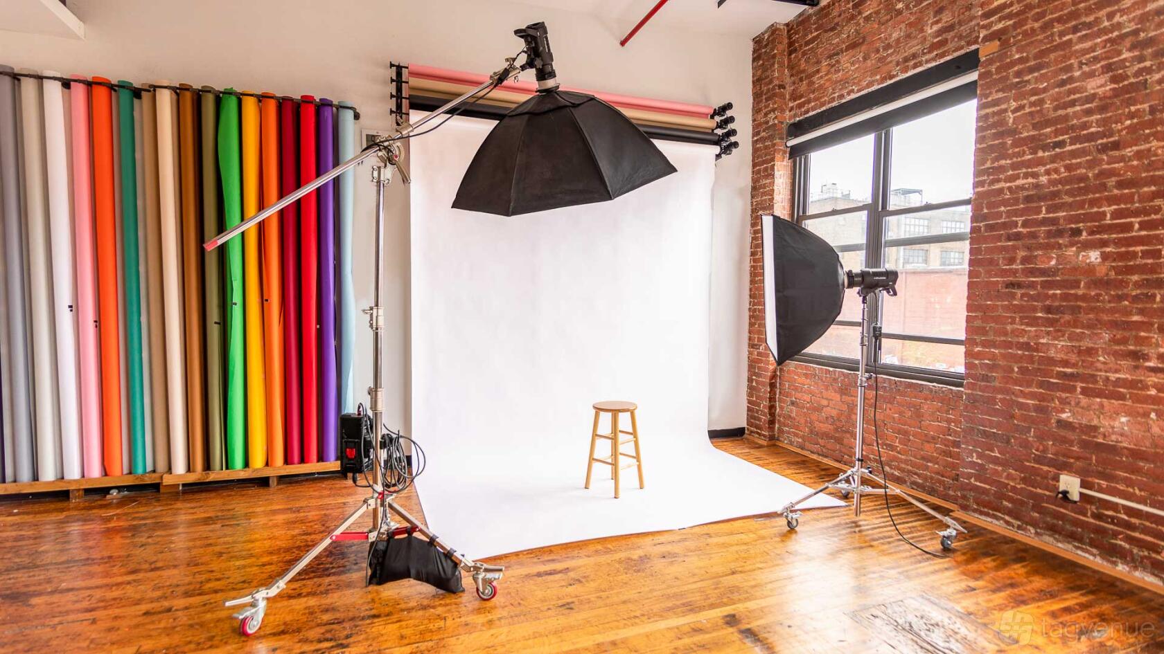 A photo studio with seamless white backdrop, studio lights, exposed brick walls, and hardwood floors at All Inclusive East Williamsburg Photo Studio.