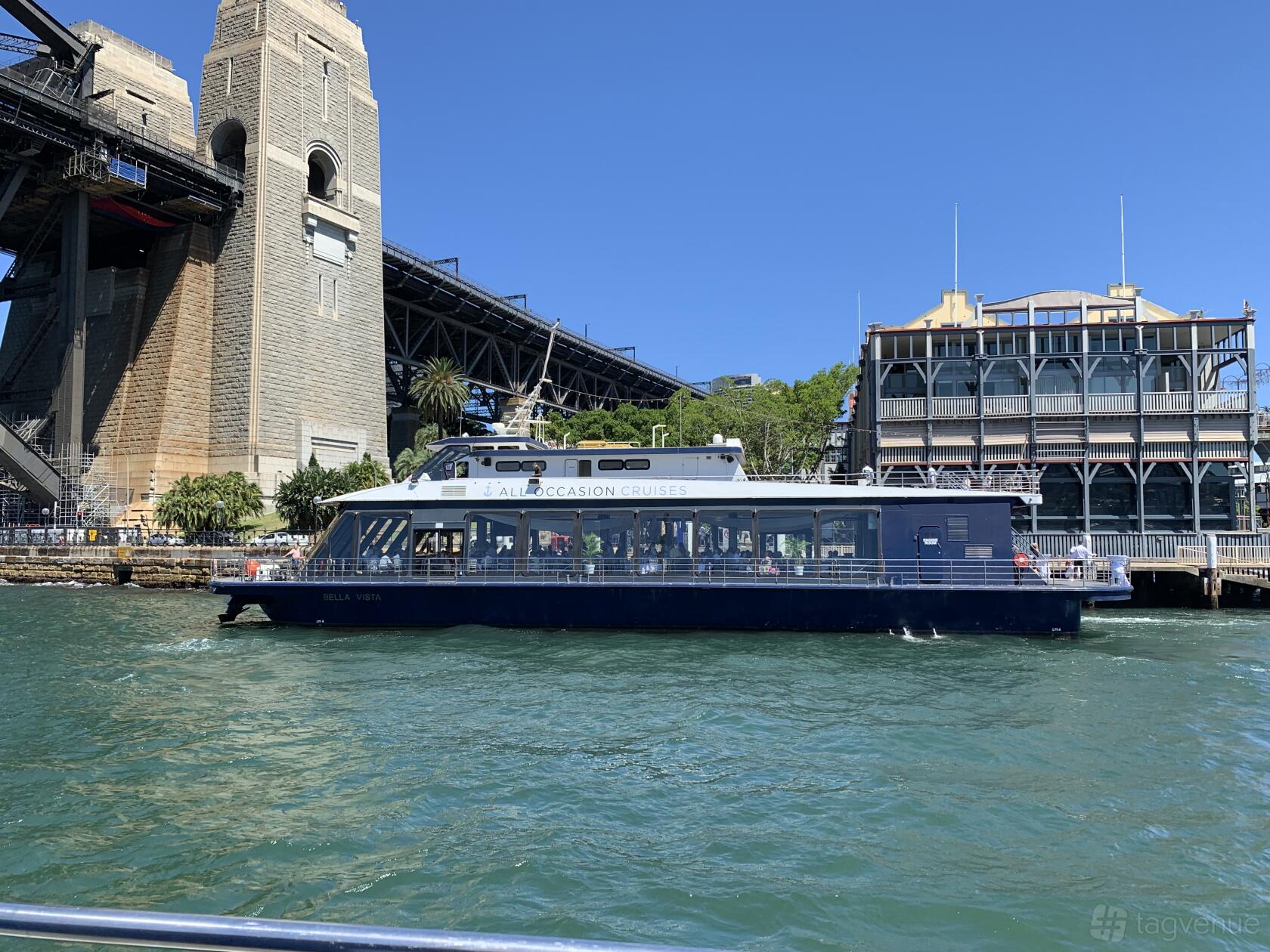 A boat with large windows cruising on the harbor near the Sydney Harbour Bridge at All Occasion Cruises.