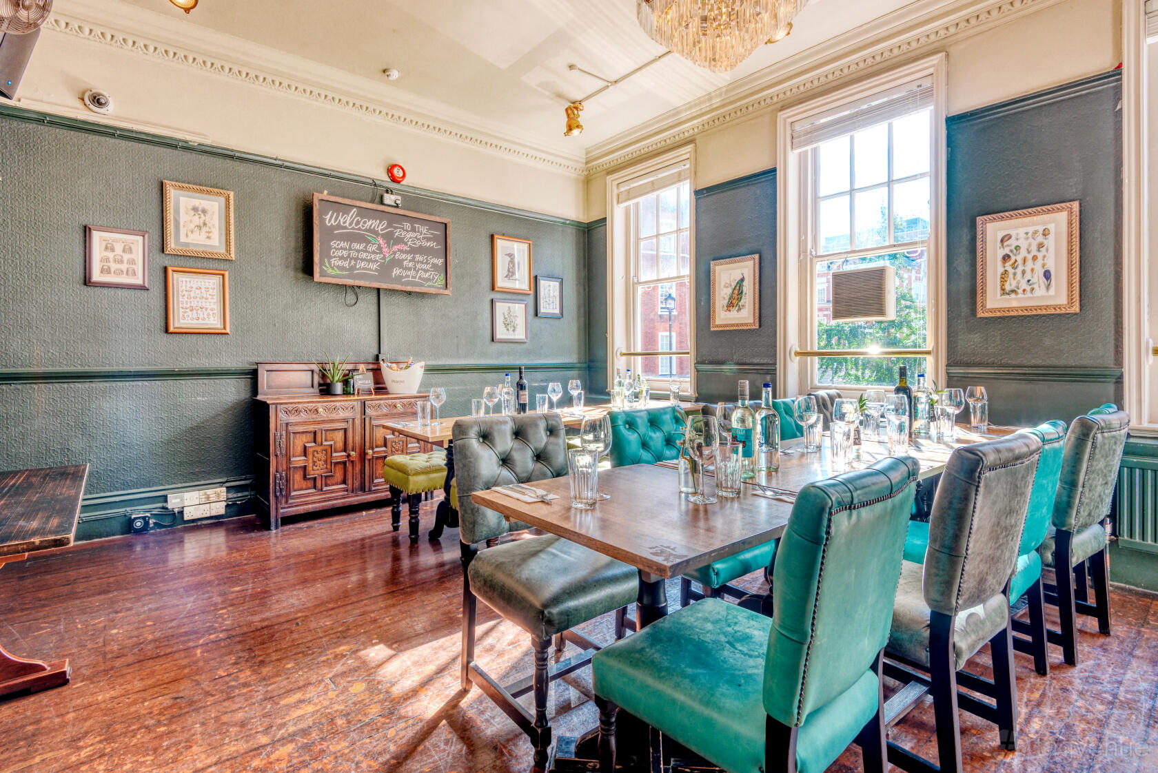 A function room with tufted green chairs, framed wall art, and large windows at The Prince Regent.