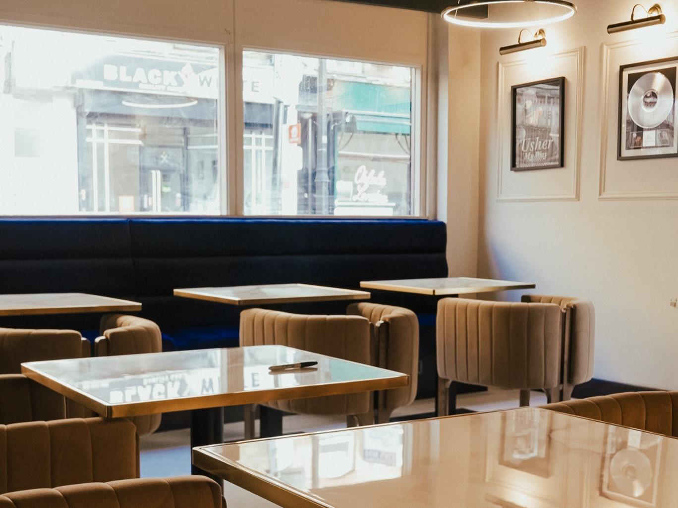 A restaurant with velvet upholstered chairs, square tables, and large front windows at OSR Restaurant & Bar.