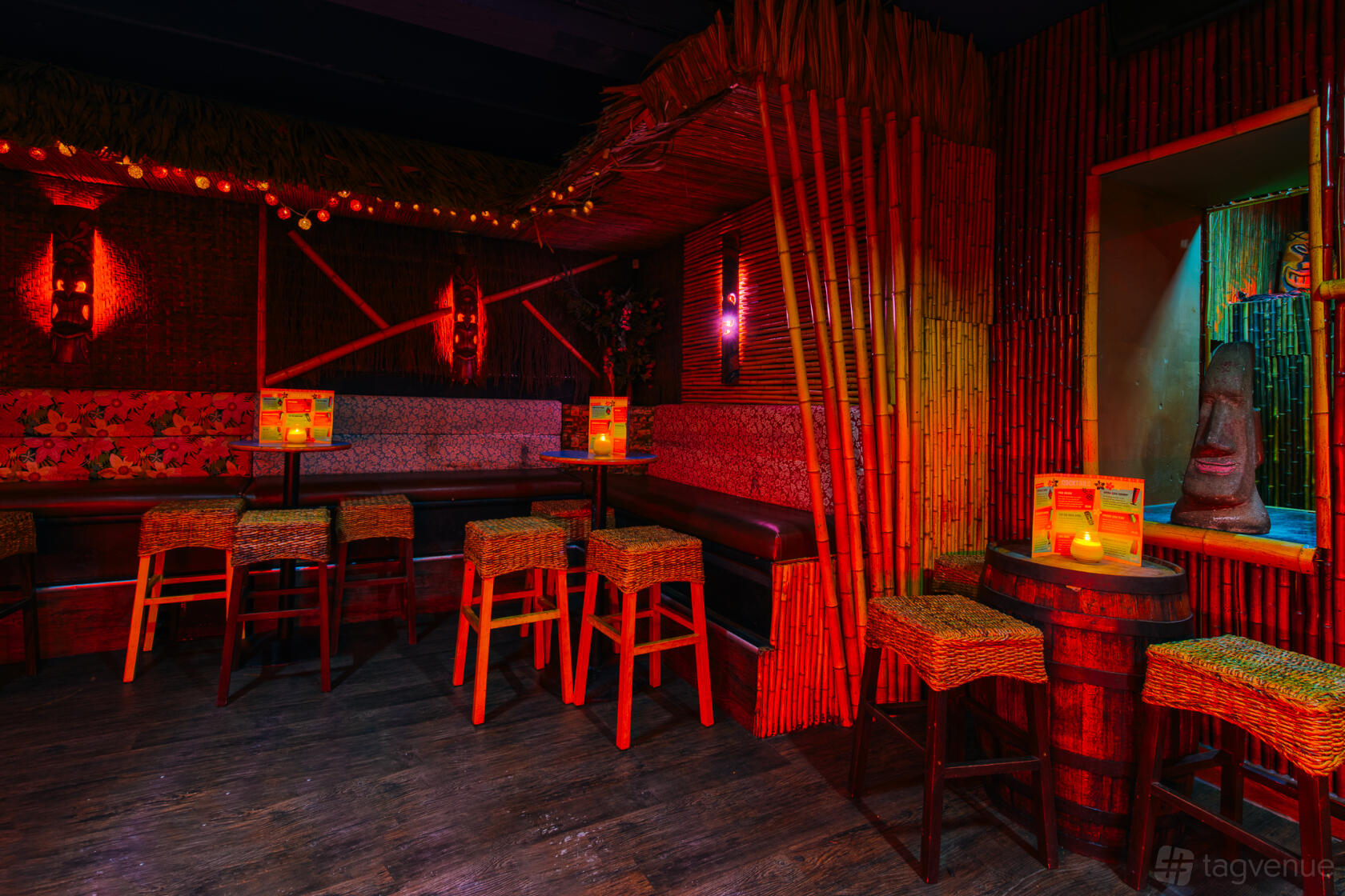A tiki bar with bamboo walls, woven stools, red ambient lighting, and island-themed decor at Tiki Hideaway.