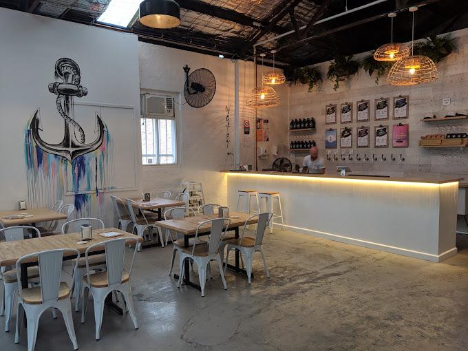 A brewery event space with wooden tables, white metal chairs, and a wall mural of an anchor at Bay Road Brewing.