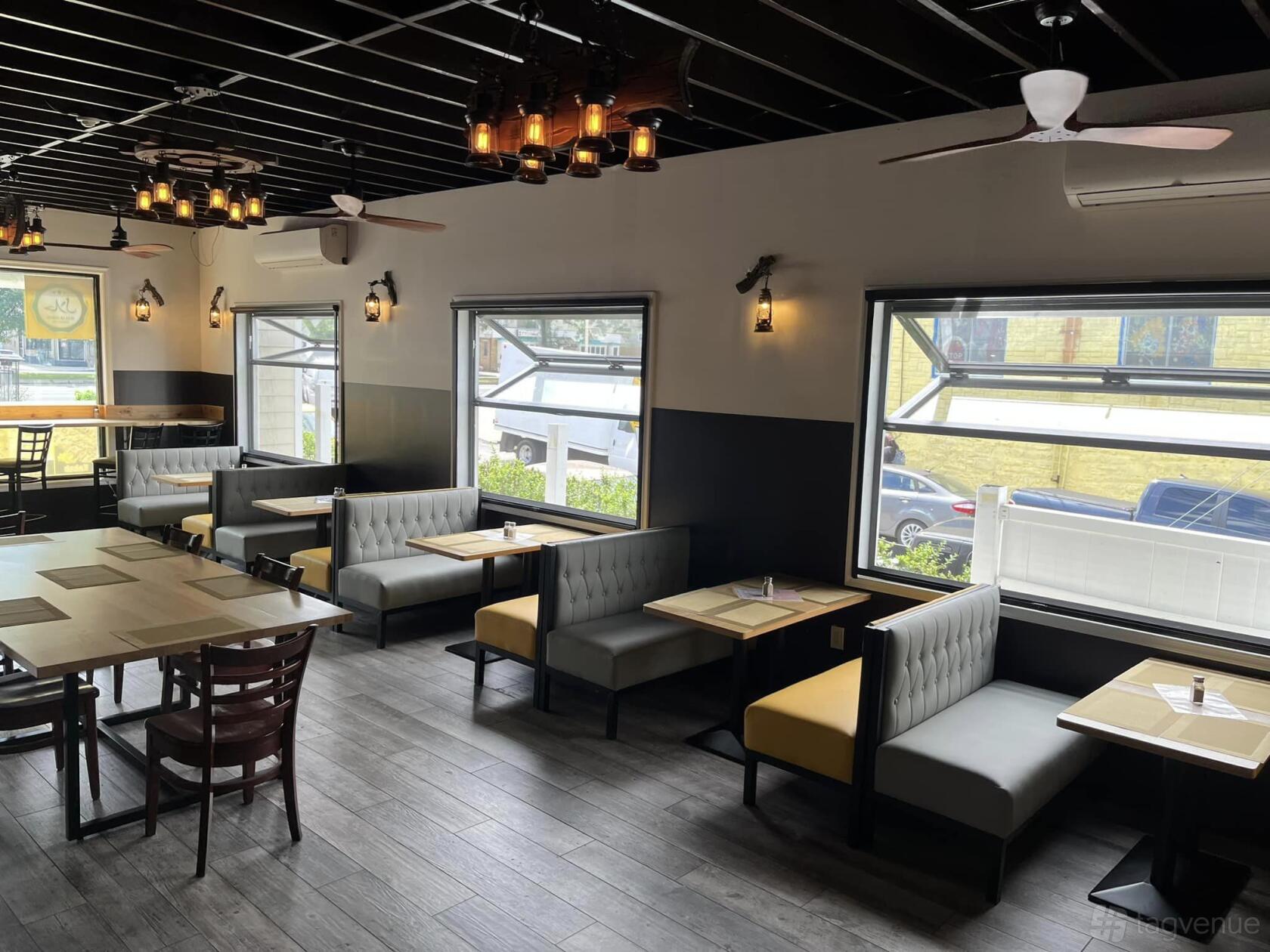 A restaurant with booth seating, large windows, wood flooring, and pendant lighting at Lobongo Kabab and Cafe.