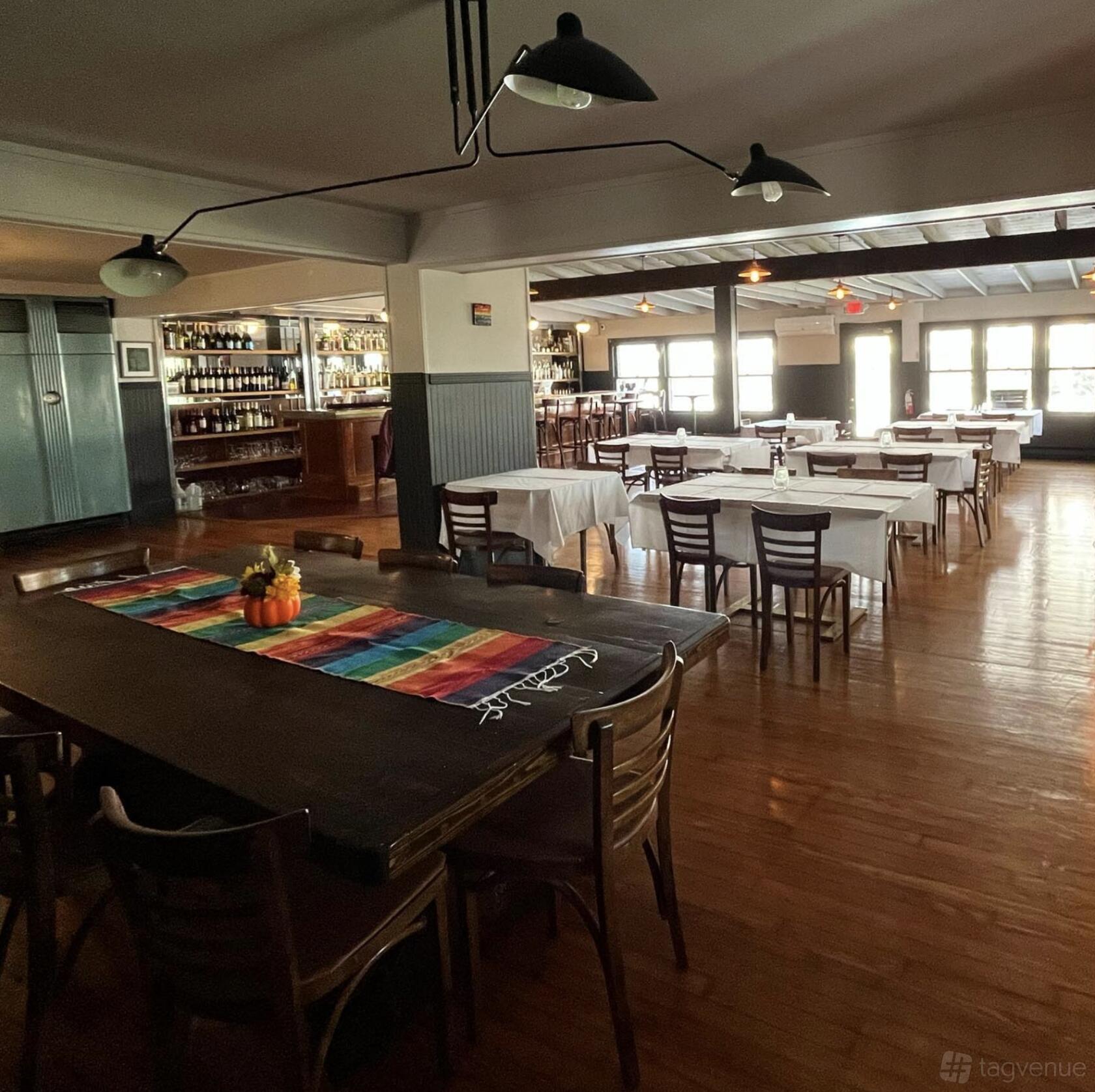 A restaurant with wooden floors, a long table with a colorful runner, and shelves of liquor bottles at Rainbow Mountain Resort.