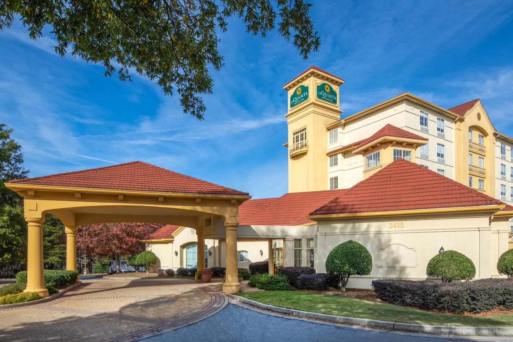 A hotel entrance with a covered driveway, manicured bushes, and a multi-story building at La Quinta Inn & Suites Atlanta Ballpark.