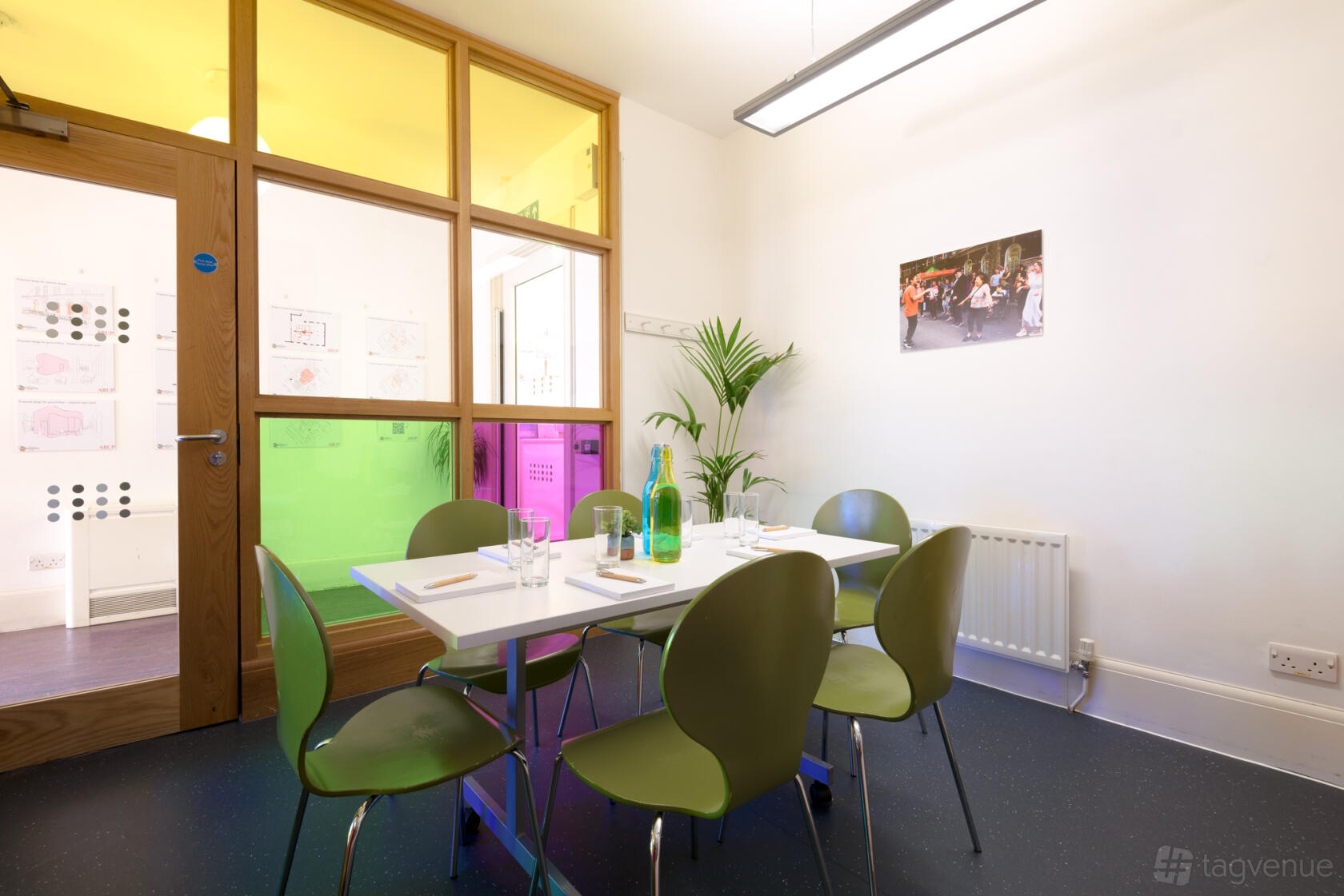 A meeting room with six green chairs, a white table, and colorful glass panels at Fitzrovia Community Centre.