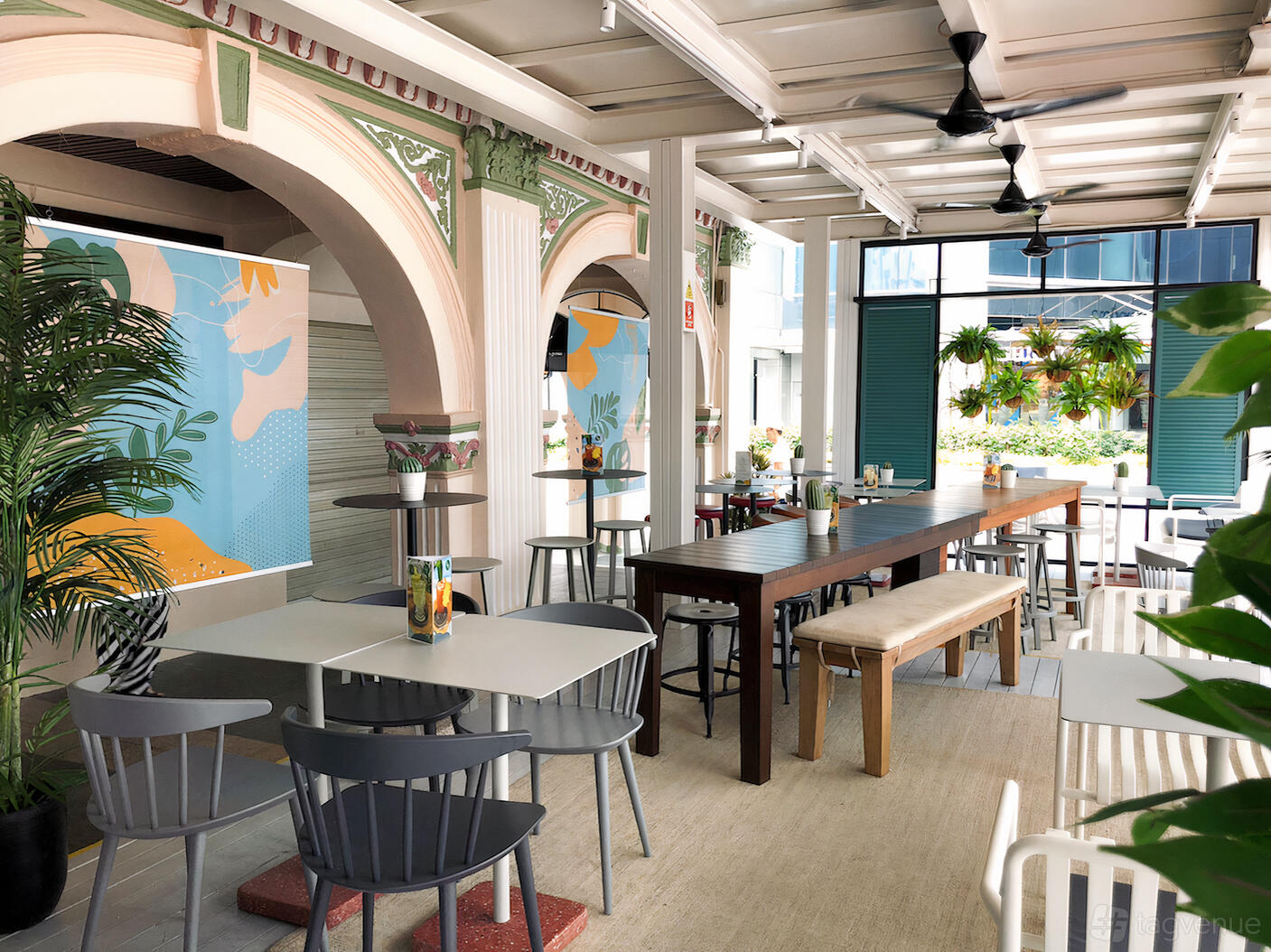 An event space in a restaurant with ceiling fans, long wooden tables, and colorful arches at Acid Bar.
