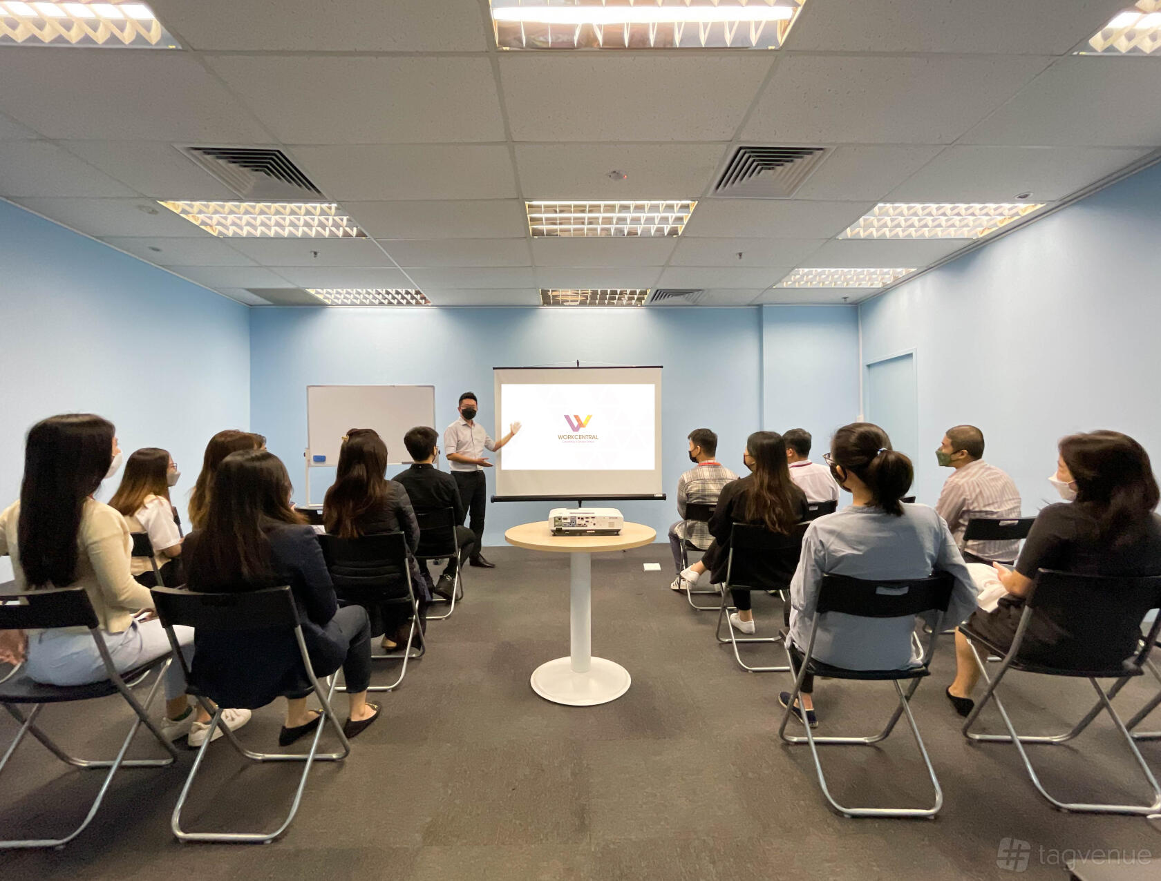 A coworking space with a projection screen, folding chairs, and fluorescent lighting at Workcentral.