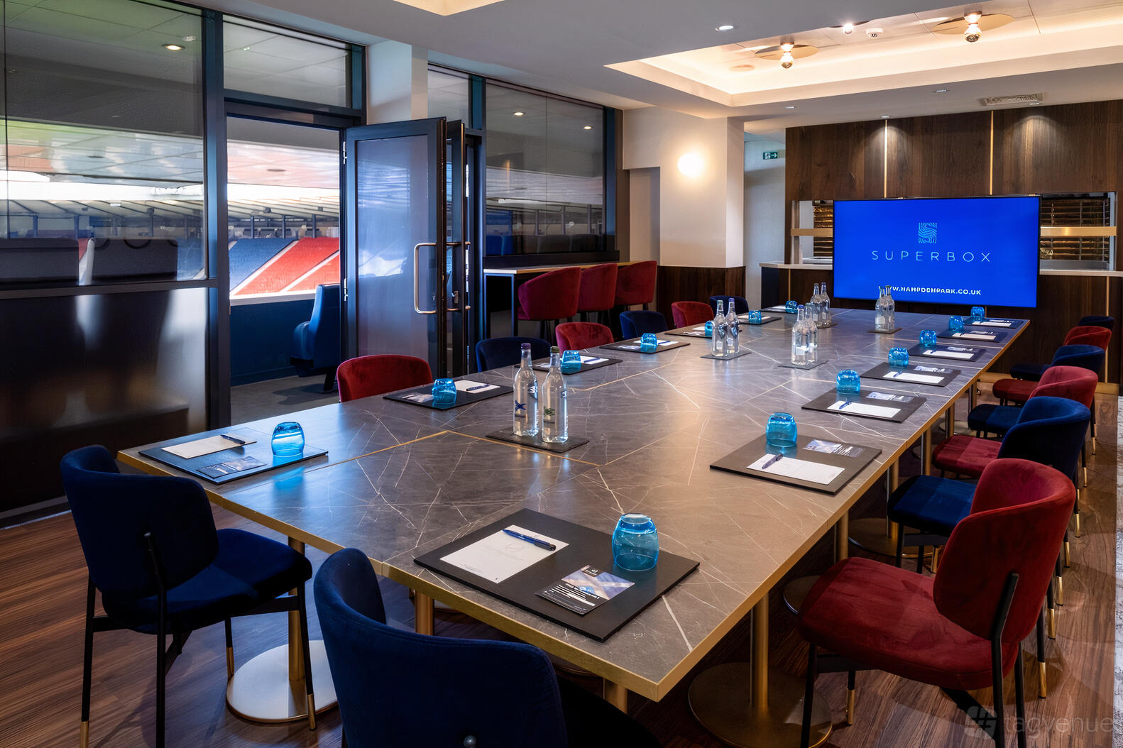 A meeting room with a long marble conference table, colorful velvet chairs, and stadium views at Hampden Park Stadium.