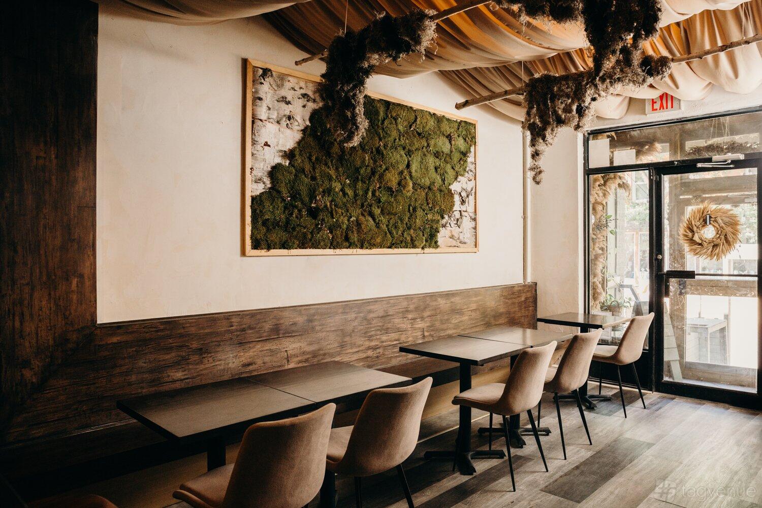 A restaurant with moss wall art, draped ceiling fabric, and light wood chairs with black tables at Hawker.