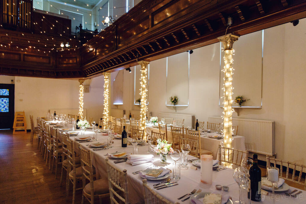 An event venue with long banquet tables, white linens, and columns wrapped in string lights at The Amadeus.