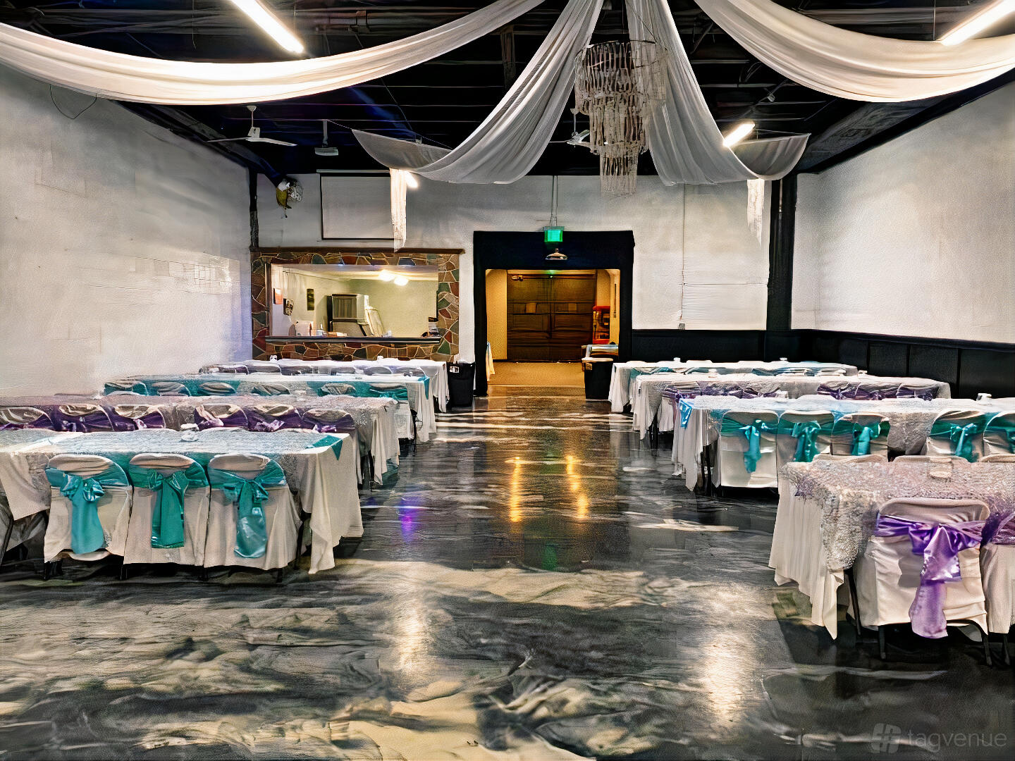 A hall with long tables draped in sequin tablecloths and colorful chair sashes beneath draped fabric ceiling at Tha Star Place.