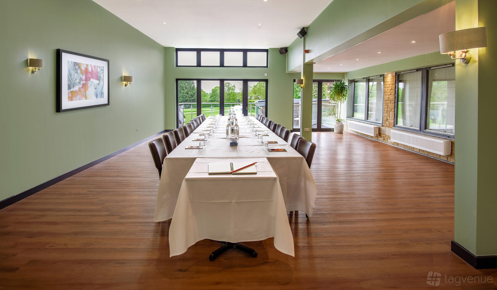 A function room with floor-to-ceiling windows, natural light, and an oval conference table at Cotswolds Hotel & Spa.