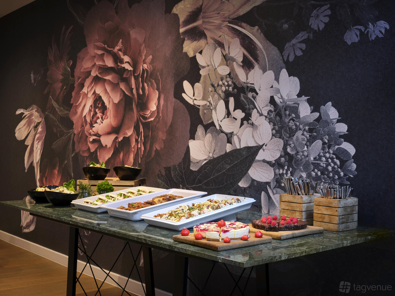 A catering table with assorted salads, pastries, and cutlery in front of a floral mural at The Westminster London.