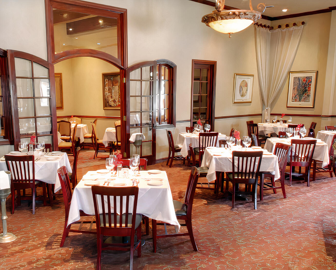 A dining room with white tablecloths, wooden chairs, framed artwork, and glass-paneled doors at Sorrento.