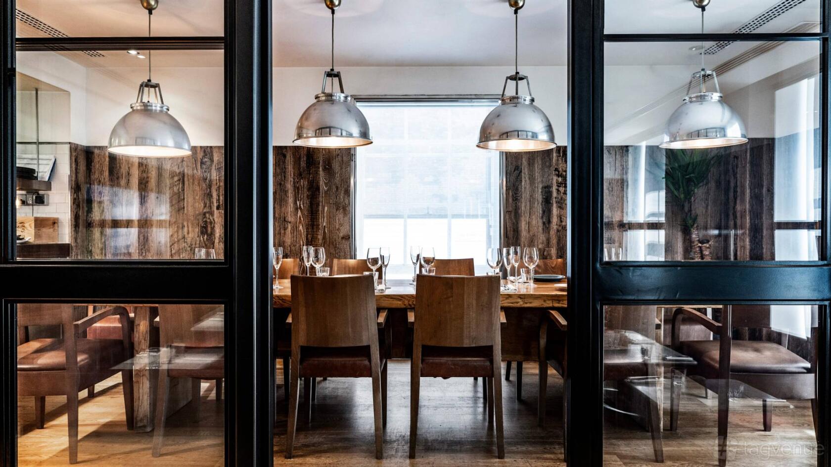 A private dining room with wood-paneled walls, pendant lighting, and a long table set with glassware at Gordon Ramsay Bar & Grill Mayfair.