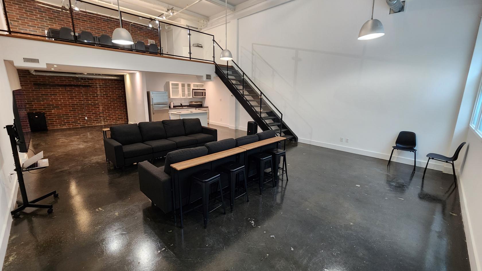 A loft with polished concrete floors, black couches, a wooden bar table, and exposed brick at It's Game Night.