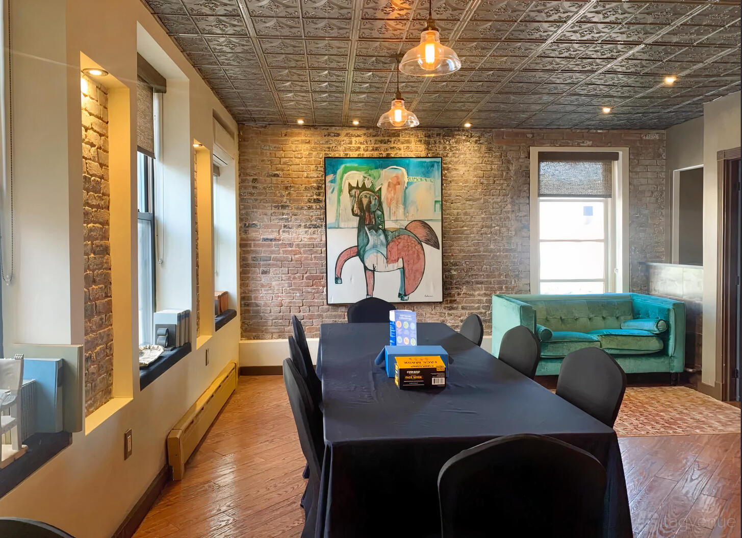 A dining room with exposed brick walls, a long table with black linens, and a green velvet sofa at Suite 500.