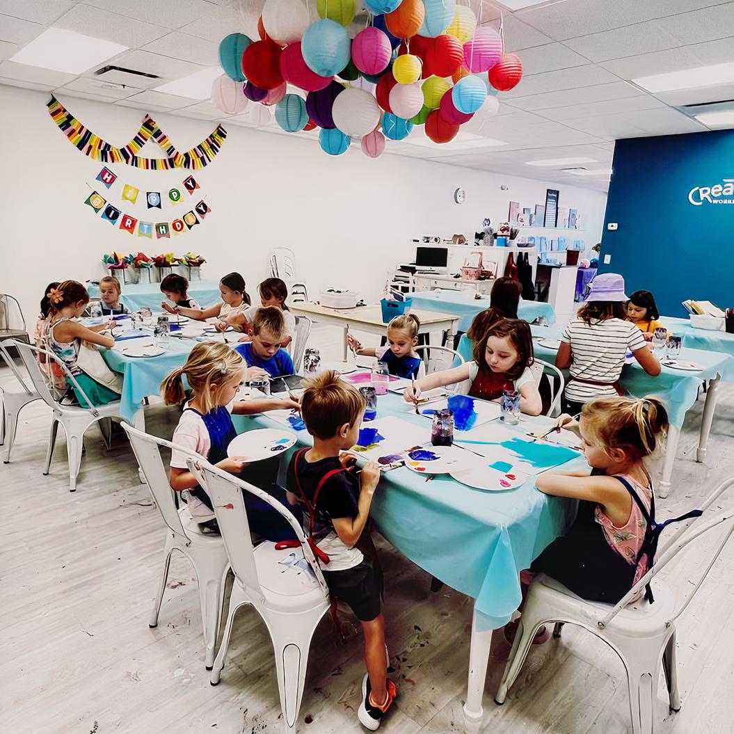 An event venue with children painting at tables covered in blue tablecloths and birthday decorations at Createry Workshop - Highlands Ranch.