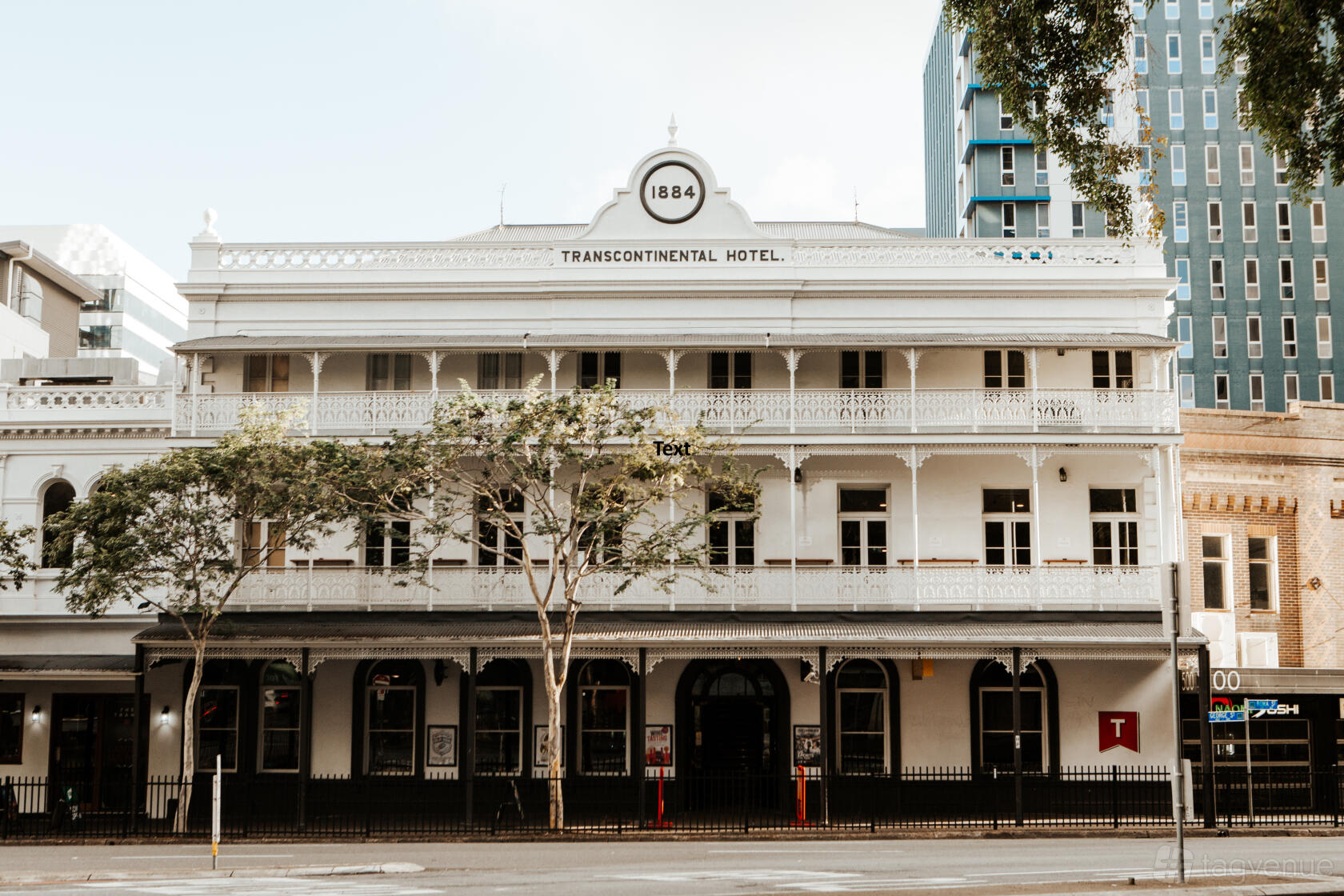 A historic pub with ornate white balconies, arched windows, and a tree-lined facade at The Transcontinental Hotel.