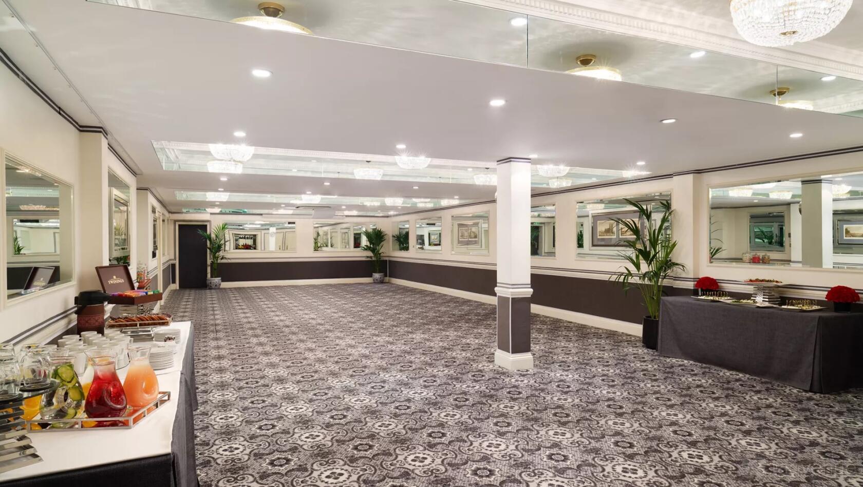 A hotel event suite with patterned carpet, mirrored walls, chandeliers, and refreshment tables at The Montague on the Gardens.
