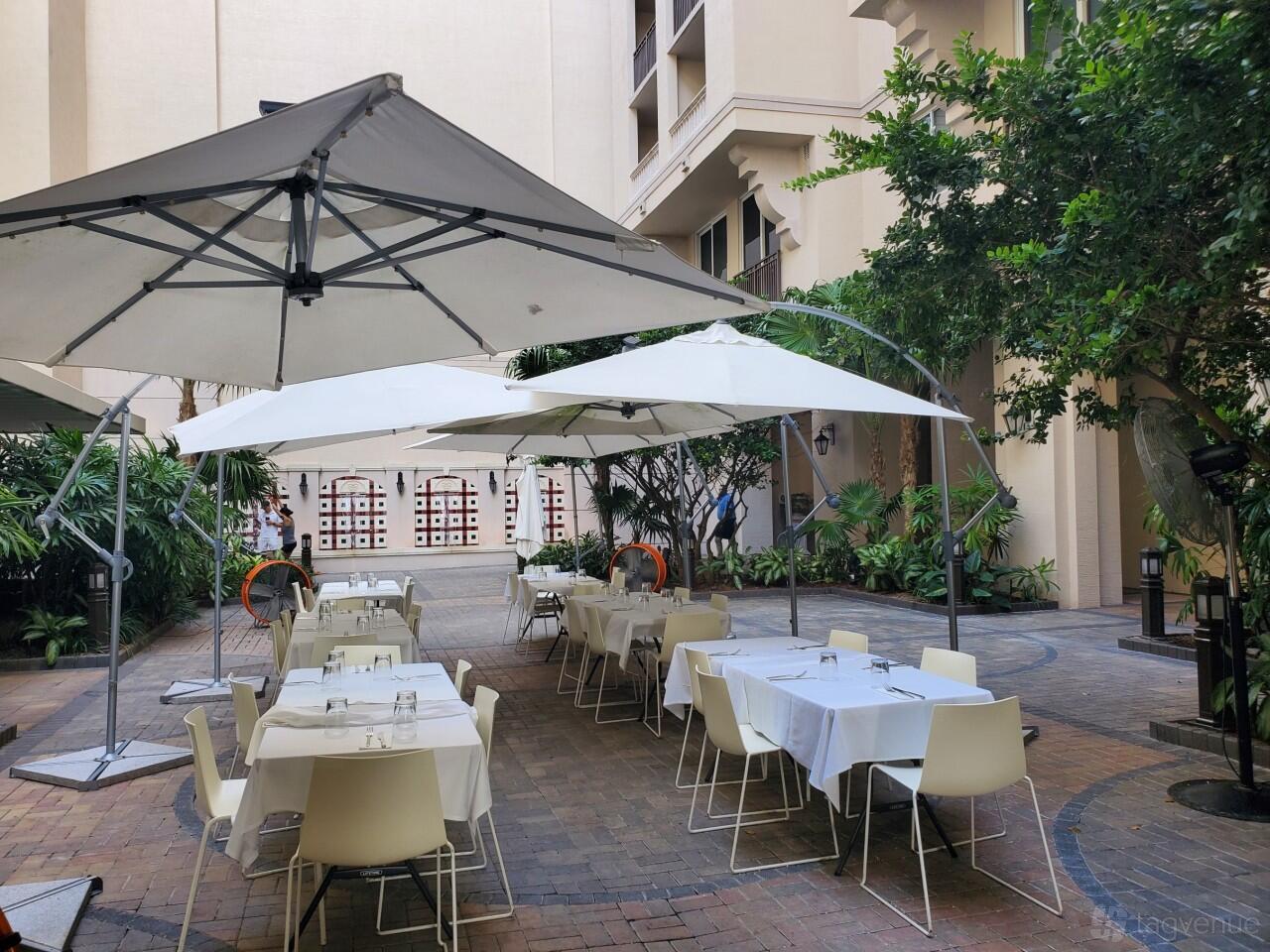 An outdoor dining area with white tables, chairs, and large umbrellas surrounded by greenery at Bachour.