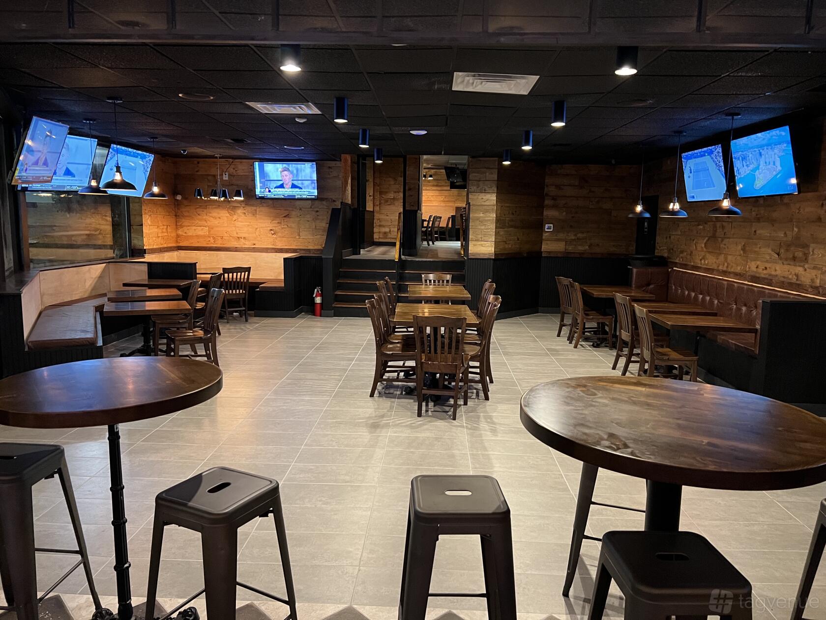 A bar with wooden tables, leather banquette seating, wall-mounted TVs, and wood-paneled walls at Home Base Delaware.