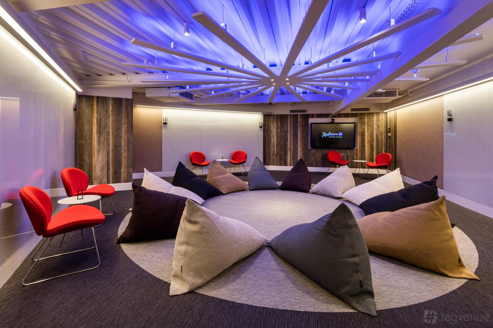 A meeting room with circular seating made of colorful bean bags, wood accent walls, and ceiling LED lights at Radisson Blu Hotel, London Heathrow.