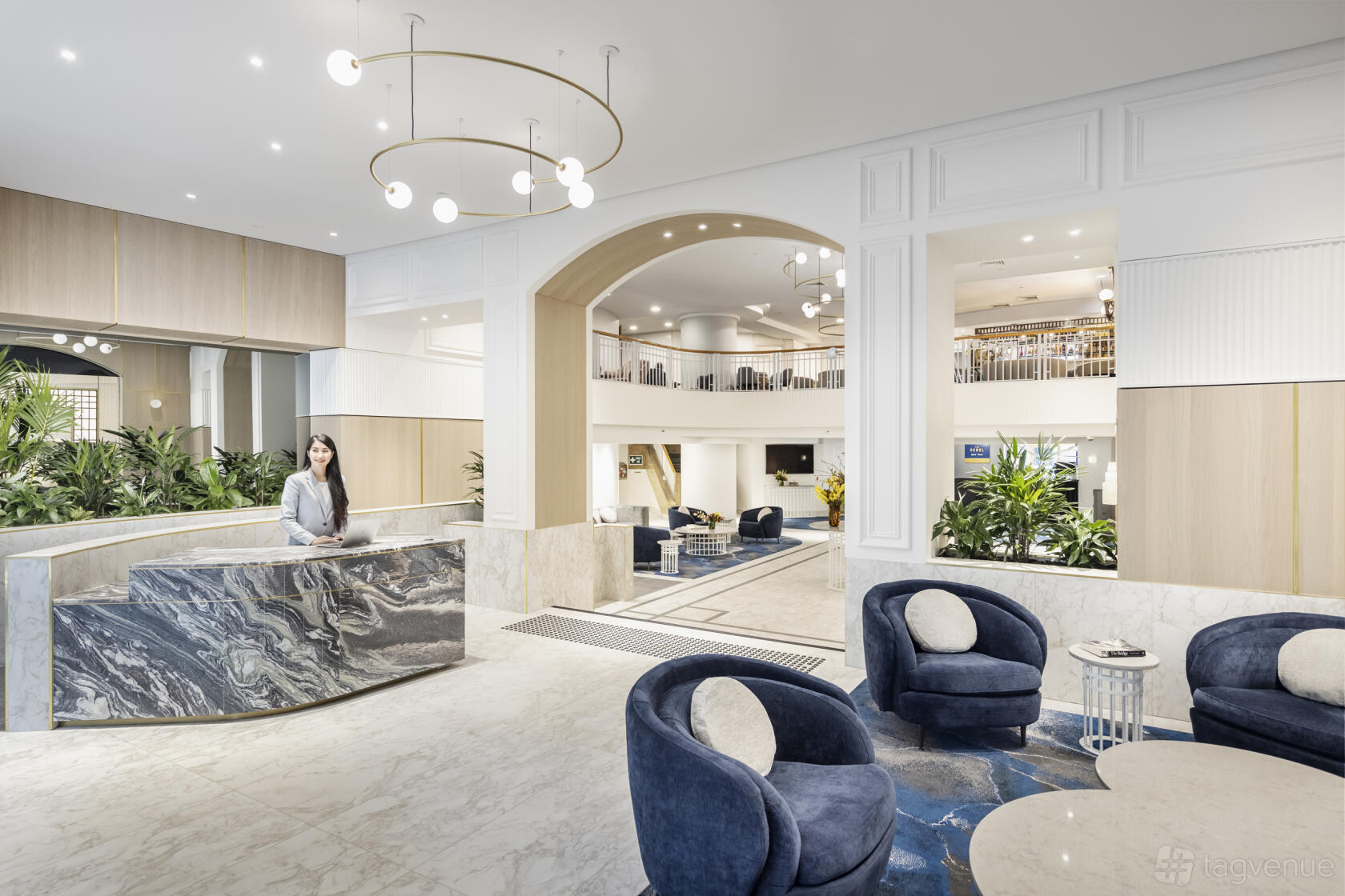 A hotel lobby with a marble reception desk, blue velvet seating, and modern globe chandeliers at Sebel Quay West Suites Sydney.