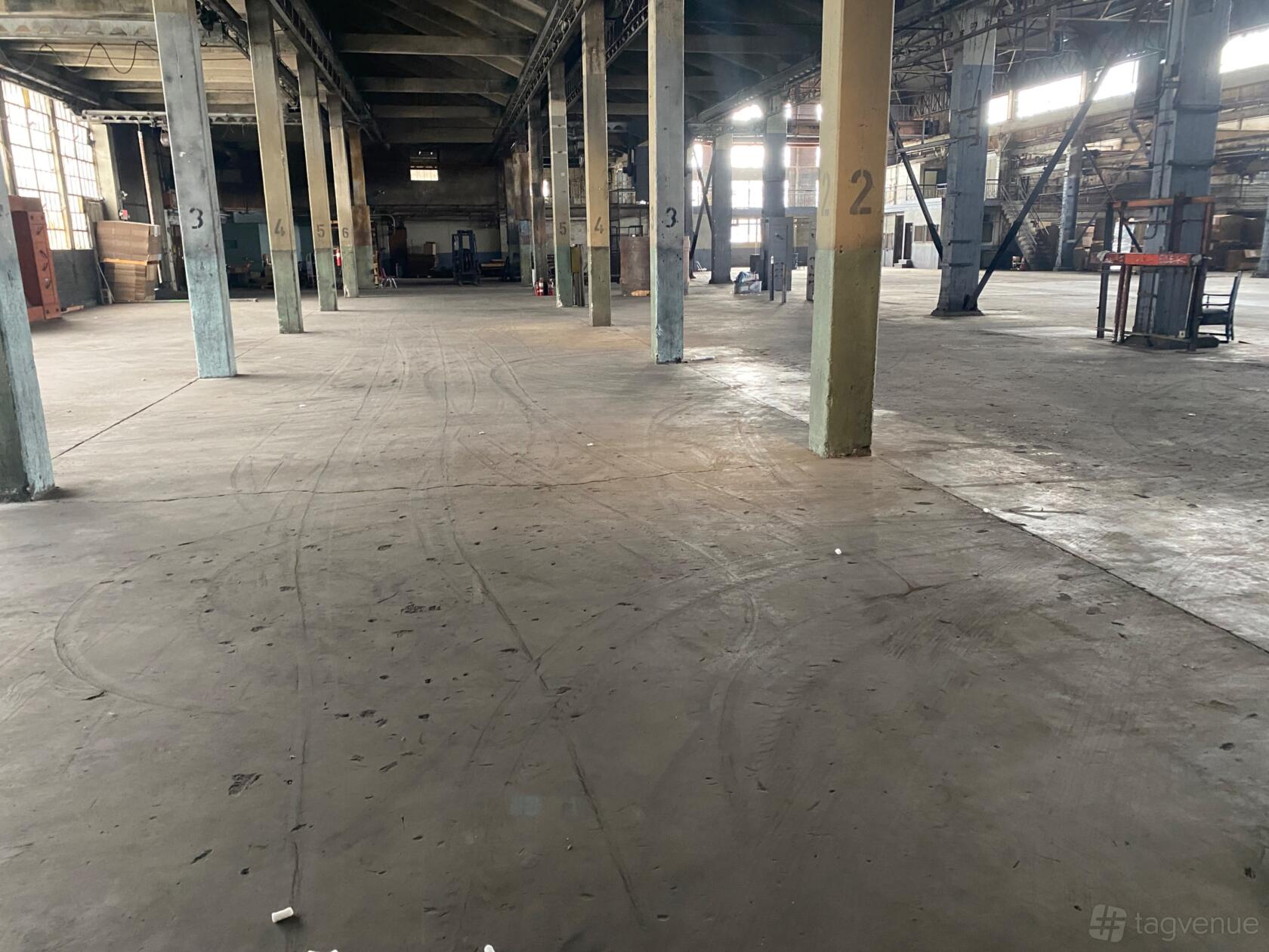 A spacious warehouse with concrete floors, high ceilings, support columns, and large industrial windows at Downtown Amazing Industrial Warehouse.