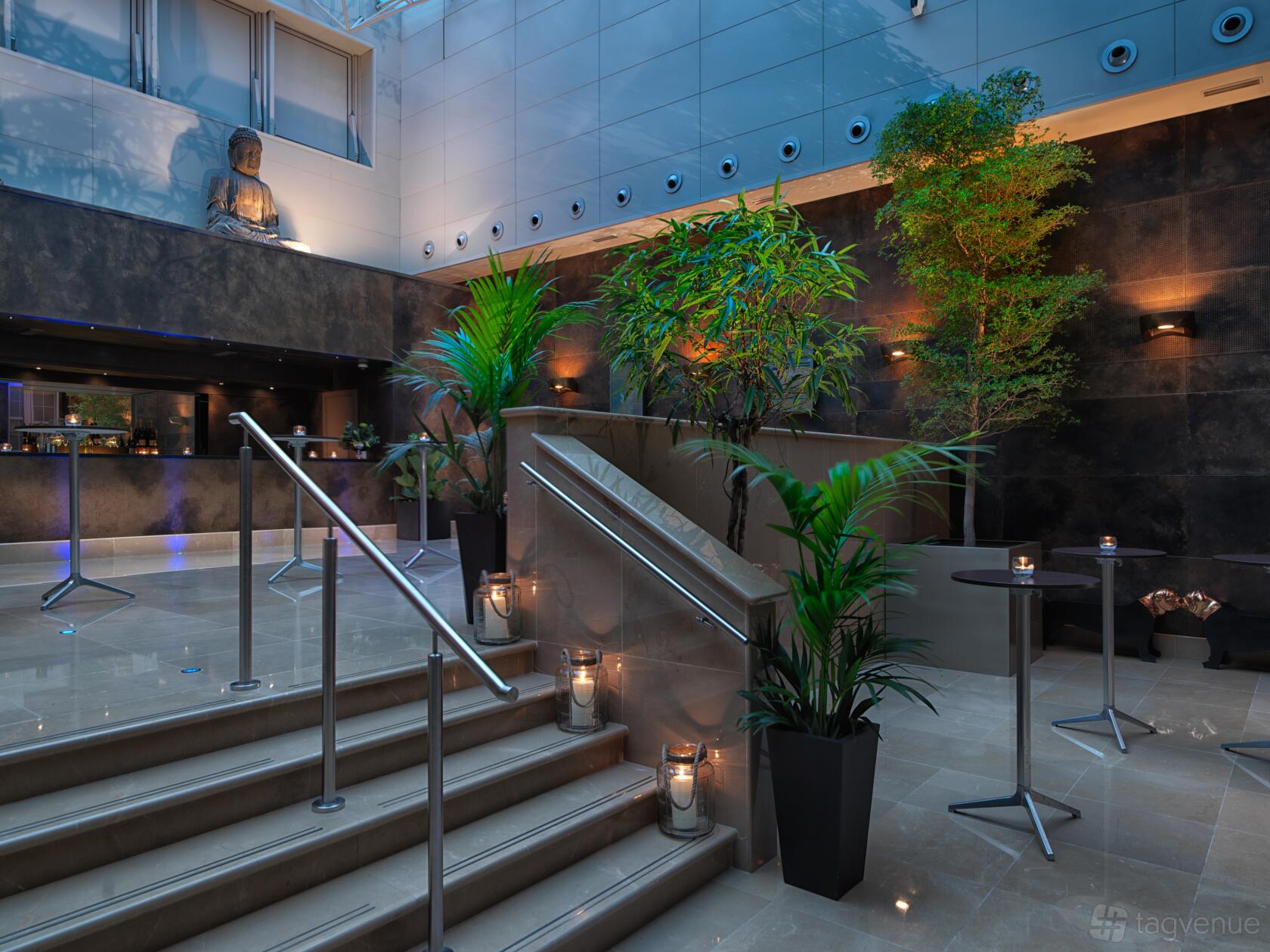 An indoor event space with potted plants, staircases, and a Buddha sculpture at The May Fair Hotel.