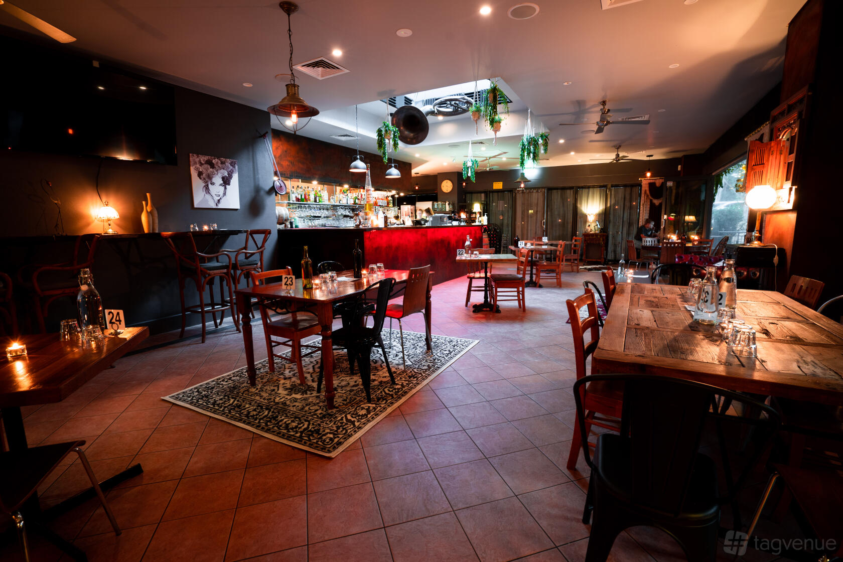 A restaurant with wooden tables, eclectic chairs, dim lighting, and a patterned rug by the bar at 3 Doors Down.