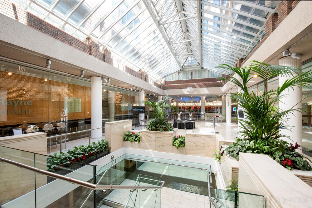An event venue with a glass atrium roof, indoor plants, and open staircases at 1 Wimpole Street.