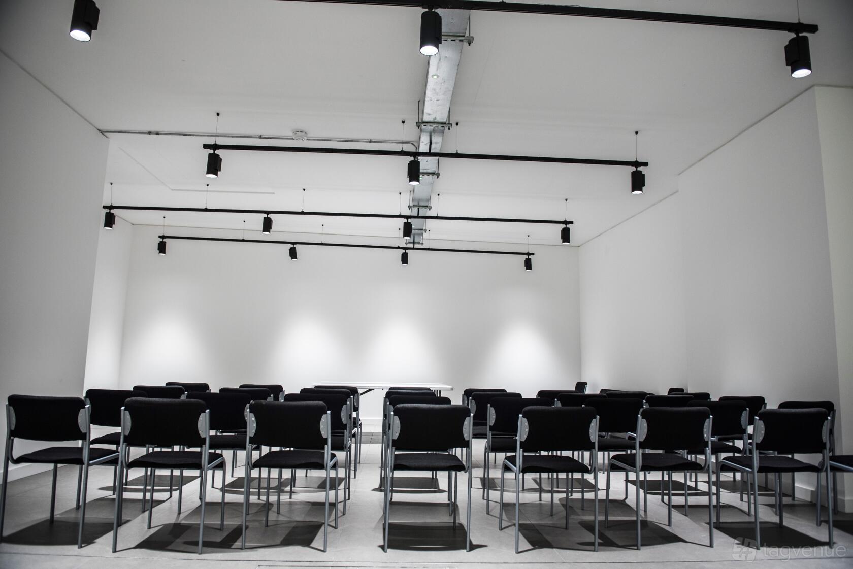 An event venue with black chairs arranged in rows, white walls, and ceiling spotlights at The White Room.