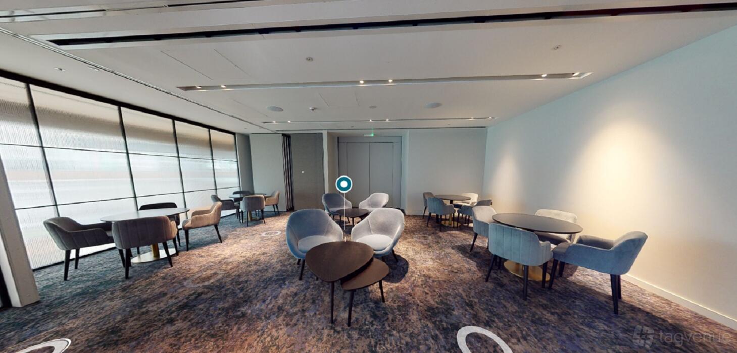 An event space with round tables, modern gray chairs, and floor-to-ceiling glass walls at Hyatt Regency London Stratford.