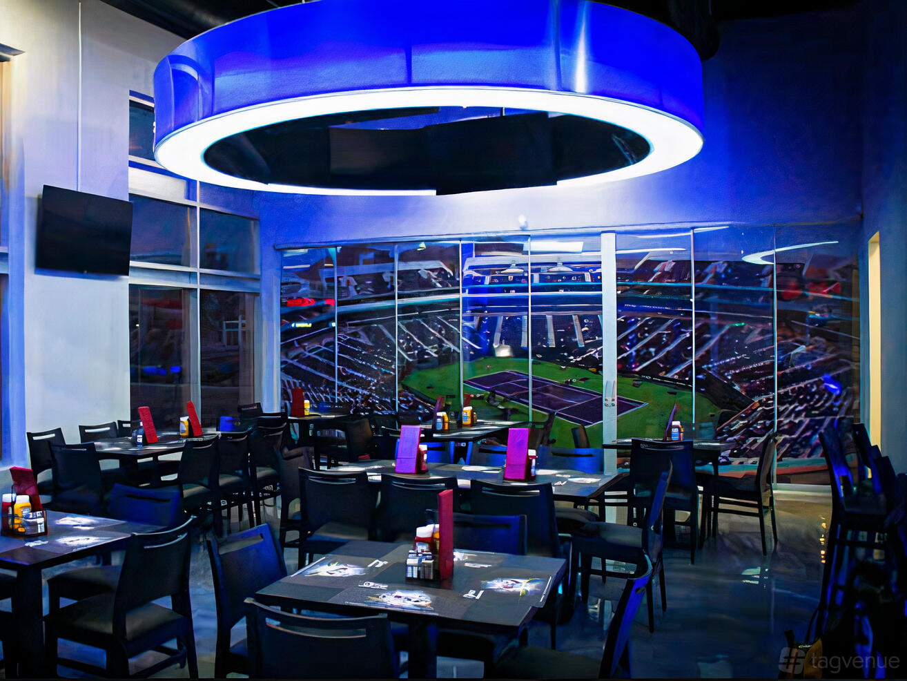 A dining room with black tables and chairs, menu holders, and a large stadium mural at Onyxx Sports Bar & Grill.