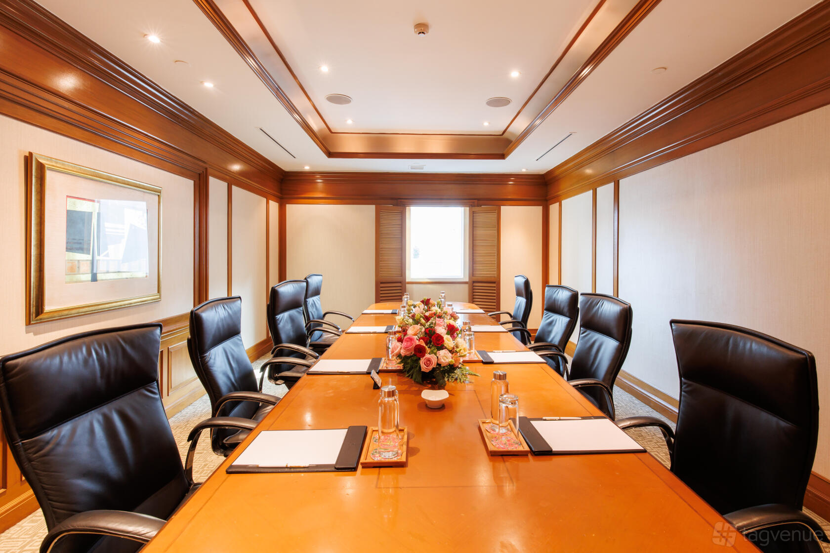 A hotel boardroom with a polished wood table, black leather chairs, and a central floral arrangement at InterContinental Singapore.