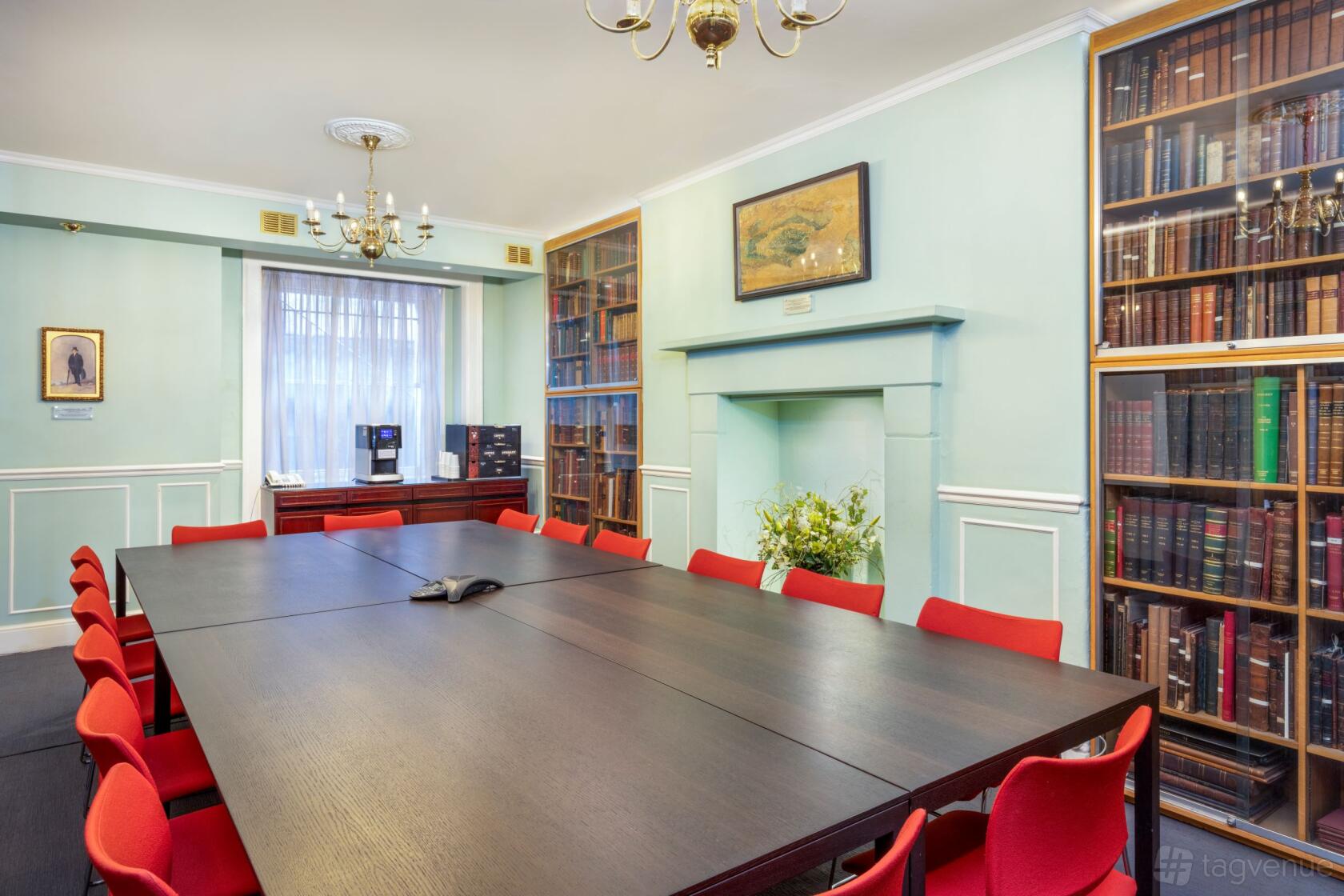 A meeting room with a dark wood table, red chairs, built-in bookcases, and chandeliers at The Geological Society.