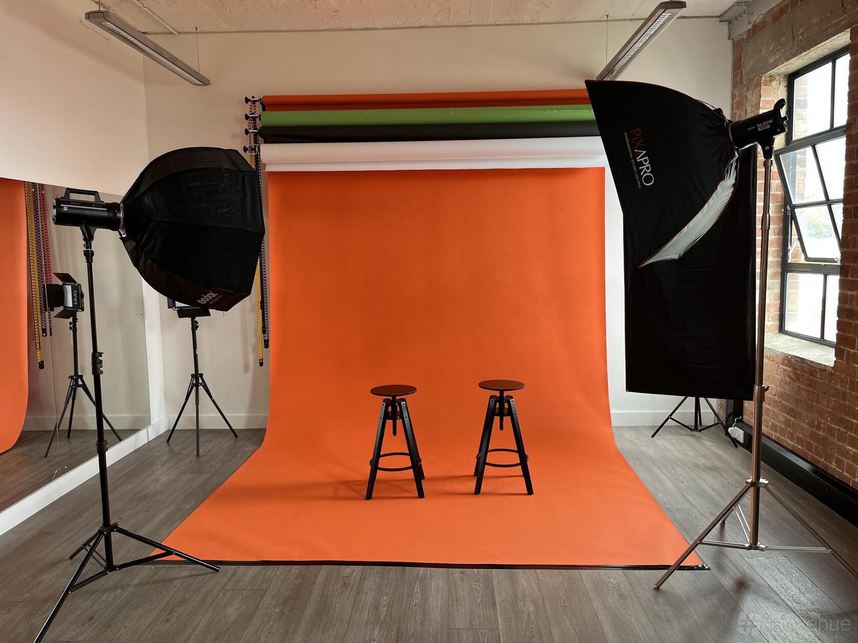 A dance studio with an orange photography backdrop, two stools, studio lights, and large windows at Creators House.