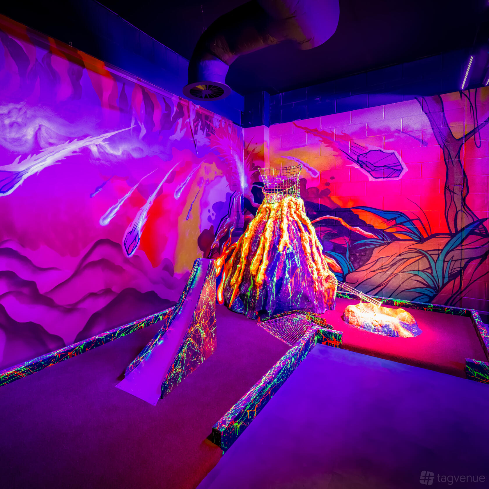A mini golf area with neon jungle-themed murals, a glowing volcano obstacle, and vibrant lighting at The Light Redhill.
