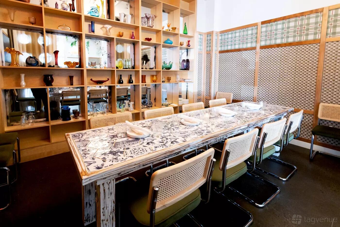 A dining room with a long patterned table, modern chairs, and built-in shelves with decorative glassware at Cafe Zuzu.