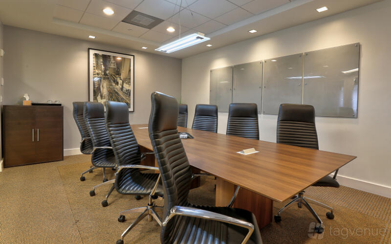 A meeting room with a long wooden conference table, high-back chairs, and a wall-mounted whiteboard at Empire Executive Offices, Fort Lauderdale.